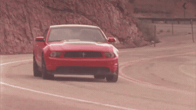 A Red Ford Mustang Is Driving Down A Road GIF