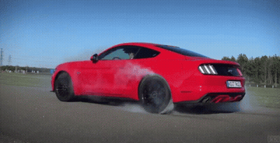 A Red Ford Mustang Is Driving Down A Road With Smoke Coming Out Of It GIF