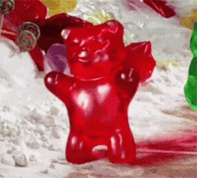 A Red Gummy Bear Standing In Front Of A Pile Of Candy GIF