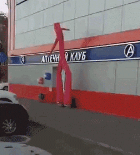 A Red Inflatable Person Is Standing In Front Of A Building With The Letter A On It GIF