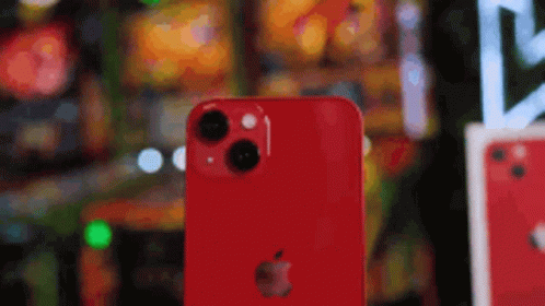 A Red Iphone Is Sitting On A Table In Front Of A Blurred Background . GIF