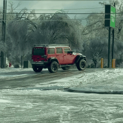 A Red Jeep Is Driving Down A Snowy Road In Front Of A Green Sign GIF