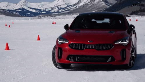 A Red Kia Car Is Parked In The Snow With Mountains In The Background GIF