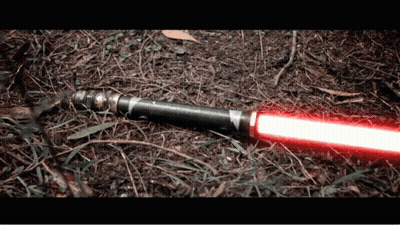 A Red Light Saber Is Laying On The Ground In The Dirt GIF