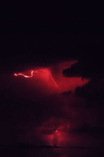 A Red Lightning Bolt Strikes The Ground In The Night Sky GIF