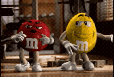 A Red M & M And A Yellow M & M Are Standing Next To Each Other In A Gym GIF