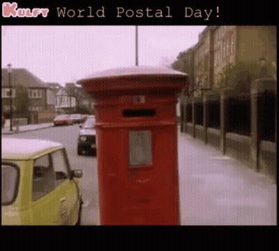 A Red Mailbox On The Side Of A Street With The Words Kulfy World Postal Day Below It GIF