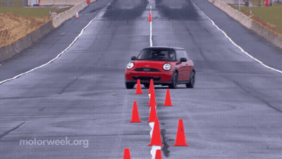 A Red Mini Cooper Is Driving On A Wet Road Surrounded By Red Cones GIF