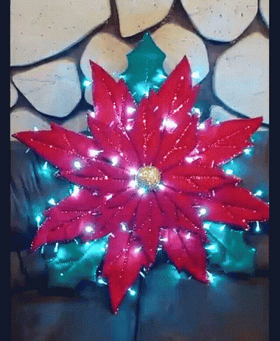 A Red Poinsettia With Christmas Lights Around It Is On A Couch . GIF