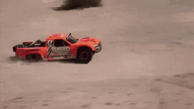 A Red Rc Truck Is Flying Through The Air On A Dirt Road . GIF