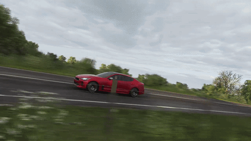 A Red Sports Car Is Driving Down A Road GIF