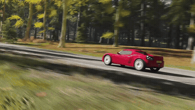 A Red Sports Car Is Driving Down A Road With Trees On The Side GIF