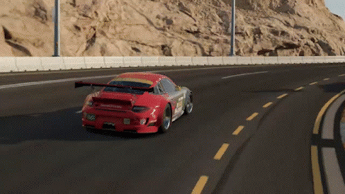 A Red Sports Car Is Driving On A Road With A Mountain In The Background GIF