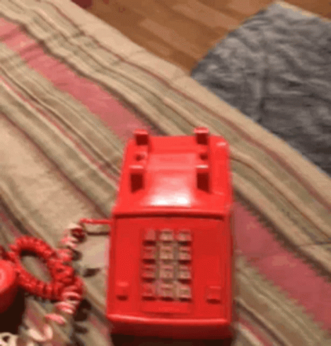A Red Telephone Is Sitting On A Bed With A Red Cord GIF