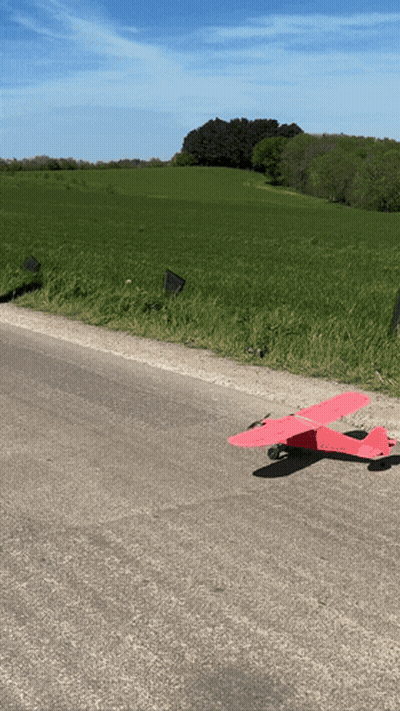 A Red Toy Airplane Is Sitting On The Side Of A Road GIF