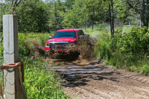 A Red Truck Drives Through A Muddy Field GIF