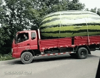 A Red Truck Is Carrying A Large Watermelon On The Back Of It . GIF