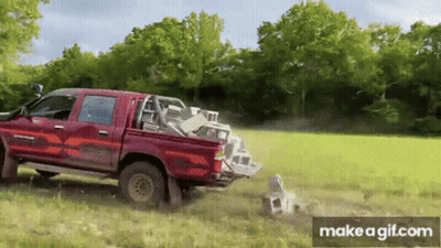 A Red Truck Is Driving Through A Grassy Field With A Pile Of Bricks In The Back . GIF