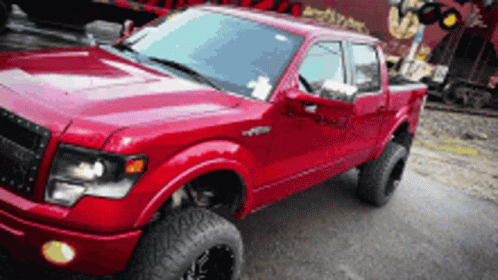 A Red Truck Is Parked On The Side Of The Road In Front Of A Train GIF