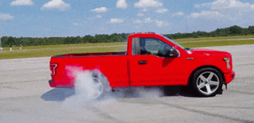 A Red Truck With Smoke Coming Out Of It 'S Tires GIF
