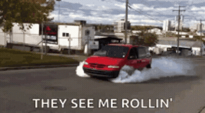 A Red Van Is Driving Down A Street With Smoke Coming Out Of The Tires And The Words They See Me Rollin GIF