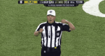 A Referee Giving A Signal On A Field With A Scoreboard Behind Him GIF