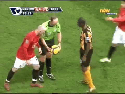 A Referee Holds A Soccer Ball Between Two Soccer Players During A Game Between Man Utd And Hull GIF