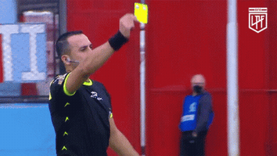 A Referee Holds Up A Yellow Card In Front Of A Red Wall With The Letters Lpf On It GIF