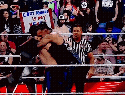 A Referee Is Standing In A Wrestling Ring Holding A Sign That Says `` Cody Rhodes Is My Hero '' GIF