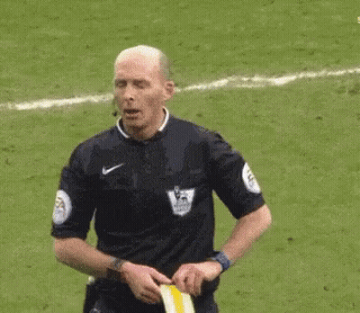 A Referee Is Standing On A Soccer Field Holding A Yellow Flag . GIF