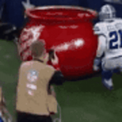 A Referee Is Taking A Picture Of A Football Player And A Large Red Pot On The Field . GIF
