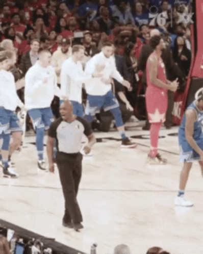 A Referee Stands On A Basketball Court Surrounded By Basketball Players GIF