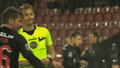 A Referee Wearing A Yellow Shirt With The Word Diadora On It Is Standing On A Soccer Field . GIF