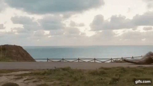 A Road Leading To The Ocean With A Fence In The Background . GIF