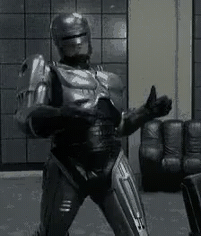 A Robot In A Suit Is Giving A Thumbs Up In A Living Room . GIF