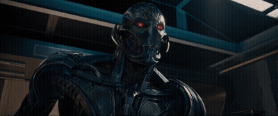 A Robot Is Standing In A Dark Room With A Blue Light Behind Him GIF