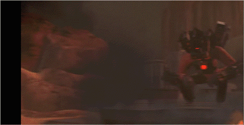 A Robot With A Red Light On The Back Is Standing In A Dark Room GIF