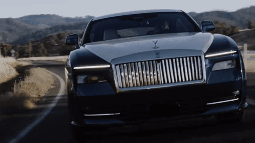 A Rolls Royce Car Is Driving Down A Road With Mountains In The Background GIF