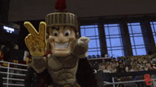 A Roman Soldier Mascot Is Giving A Peace Sign In Front Of A Crowd GIF