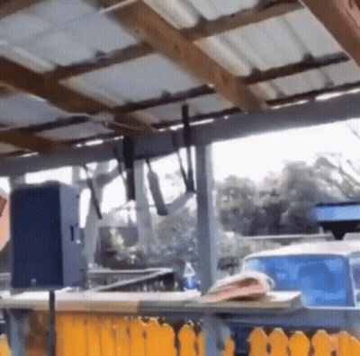 A Roof With A Few Pieces Of Wood Hanging From It And A Table With Bottles Of Orange Juice On It . GIF