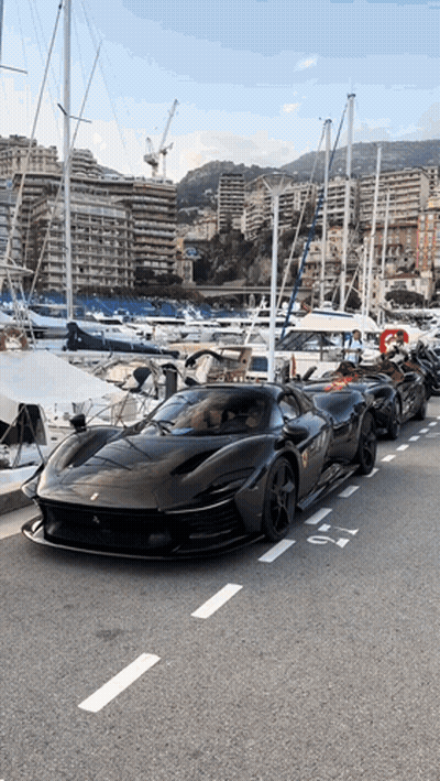 A Row Of Black Sports Cars Are Parked On The Side Of The Road Near A Marina GIF