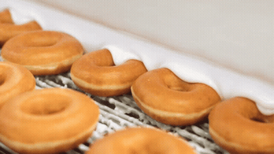 A Row Of Glazed Donuts With White Frosting On A Conveyor Belt GIF