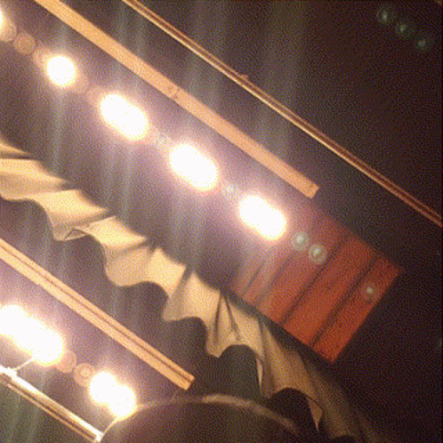 A Row Of Lights Are Shining On A Stage With A Curtain Behind Them GIF
