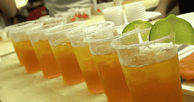 A Row Of Plastic Cups Filled With Orange Liquid And Lime Slices On A Table GIF