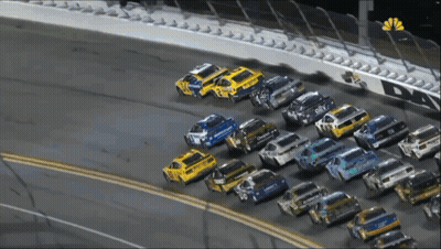 A Row Of Race Cars Are Lined Up On A Race Track With A Nbc Logo In The Corner GIF