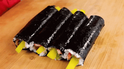 A Row Of Sushi Rolls With Yellow Onions On A Wooden Table GIF