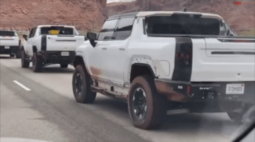 A Row Of White Trucks Are Driving Down A Highway And One Of Them Has A License Plate That Says X79h083 GIF