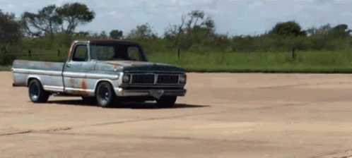 A Rusty Old Truck Is Driving Down A Dirt Road . GIF