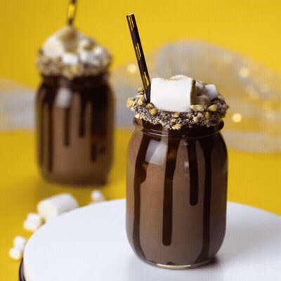 A S'mores Milkshake In A Mason Jar With Chocolate Sauce And Marshmallows GIF