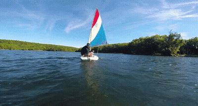 A Sailboat With A Red White And Blue Sail Is Floating On The Water GIF